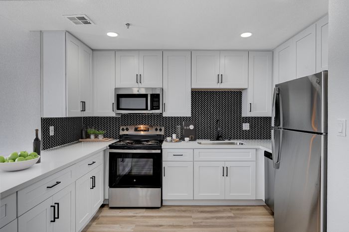 Modern kitchen with sleek white cabinetry, stainless steel appliances, and stylish herringbone backsplash.