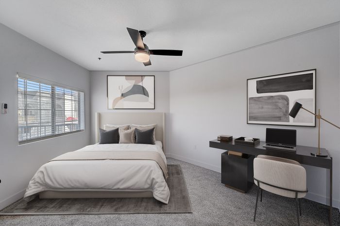 Bright and cozy bedroom with modern decor, featuring a plush bed, sleek black desk with a laptop and lamp, and elegant artwork on the walls.