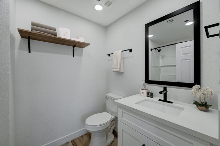 Modern bathroom with sleek white vanity, elegant black fixtures, and a large framed mirror. Minimalist design featuring open shelving and contemporary decor.