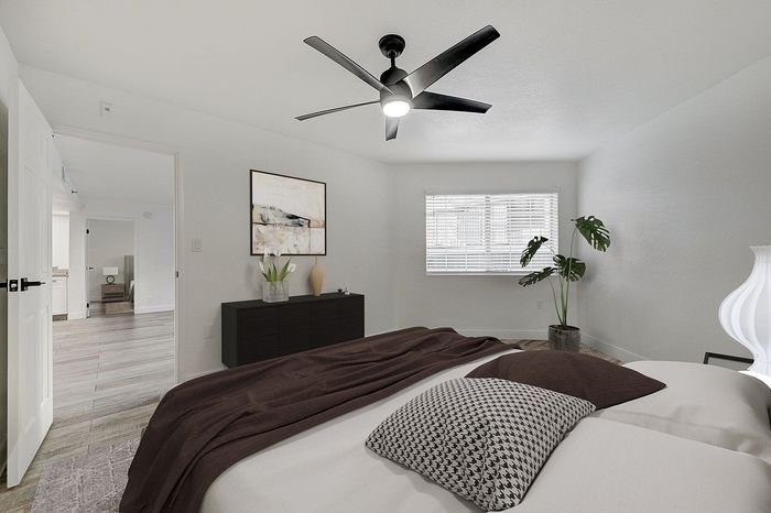 Inviting bedroom with modern decor, featuring a cozy bed, elegant ceiling fan, and abundant natural light through wide windows.