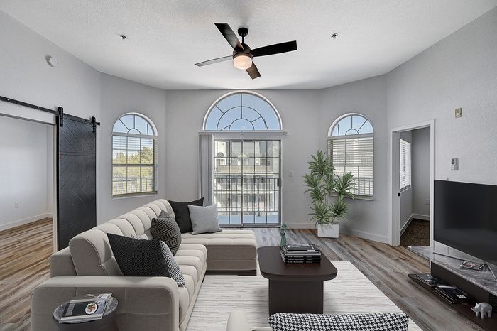 Bright and stylish living room with modern sectional sofa, large arched windows, and a sleek barn door, offering a blend of comfort and elegance.