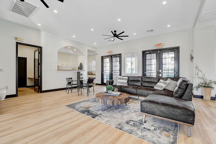 Modern living room with sleek brown sectional sofa, stylish round coffee table, elegant dining area, and abundant natural light through double doors.
