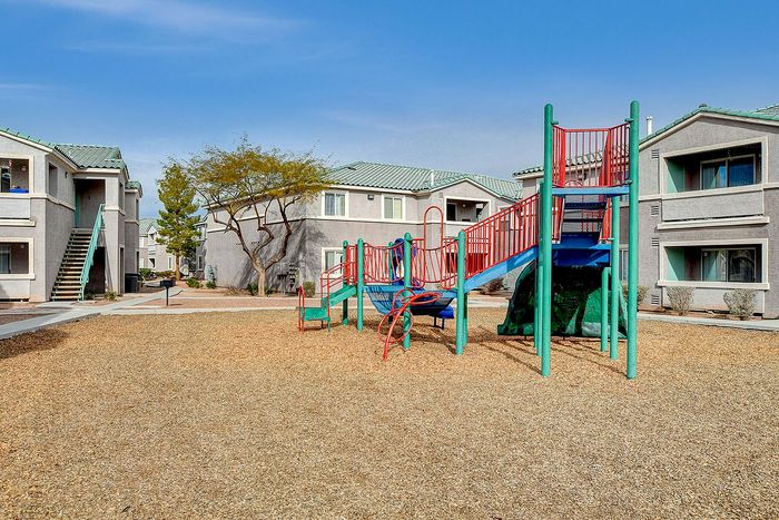Inviting apartment complex with a vibrant playground, perfect for families, surrounded by modern two-story buildings with lush greenery.