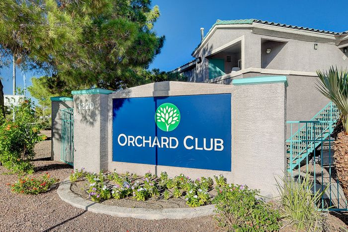 Welcoming entrance to Orchard Club Apartments, showcasing manicured landscaping and modern architecture under a clear blue sky.