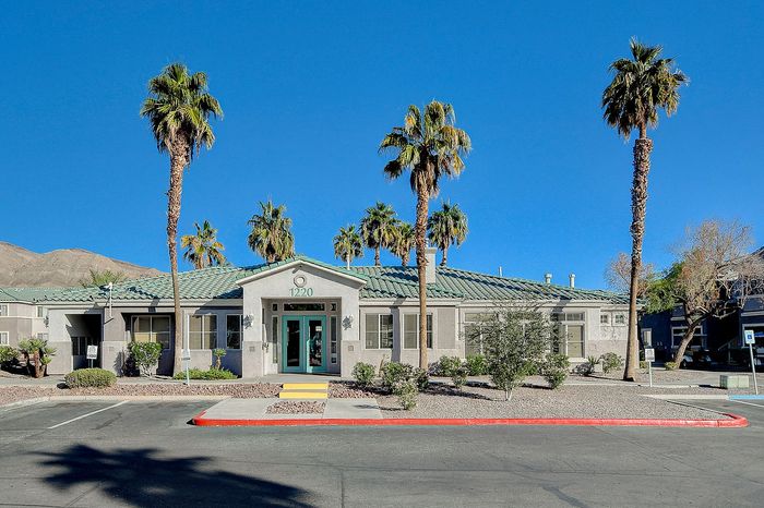 Charming residential building with modern design, surrounded by palm trees and mountain views under a clear blue sky.