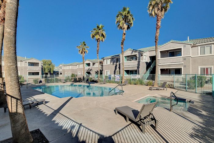 Relaxing apartment complex with modern swimming pool, surrounded by lush palm trees and stylish buildings under a clear blue sky.