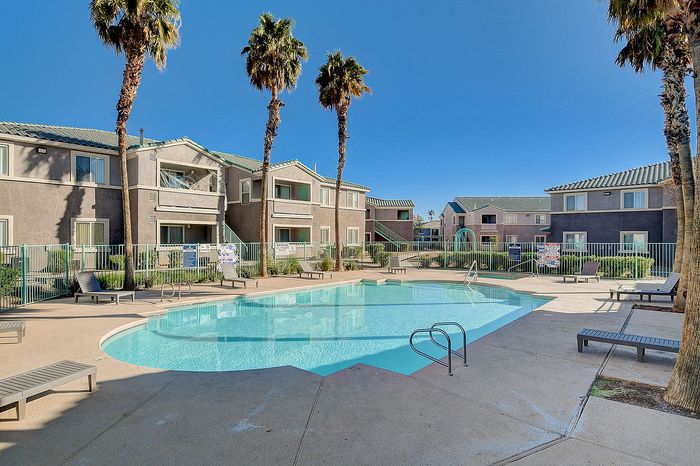 Inviting apartment complex with a sparkling pool and modern architecture, surrounded by lush palm trees and sunlit leisure spaces.