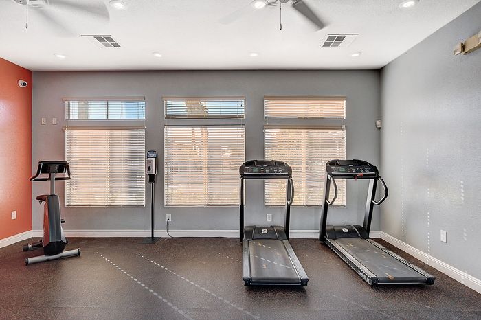 Modern fitness room featuring two treadmills and an exercise bike with large windows for natural light.