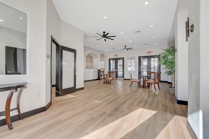 Bright and modern communal area featuring elegant wood flooring, stylish ceiling fans, and chic dining sets, perfect for gatherings.