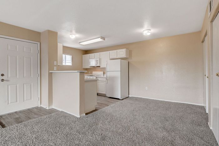 Inviting open-concept kitchen and living area featuring plush carpeting, modern white cabinetry, and ample natural light for a warm, welcoming atmosphere.