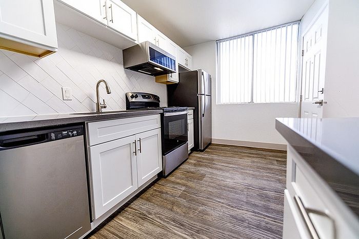 Modern kitchen with sleek stainless steel appliances, elegant white cabinetry, and stylish wood flooring for a contemporary look.