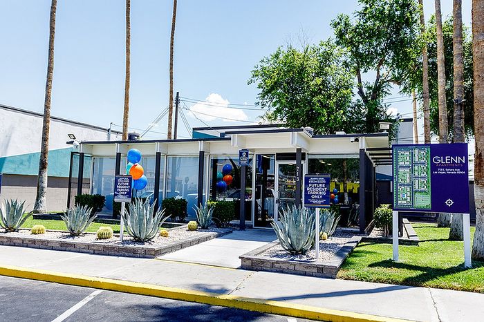 Chic entrance of Glenn Apartments with modern architecture, vibrant balloons, and lush greenery in Las Vegas setting.