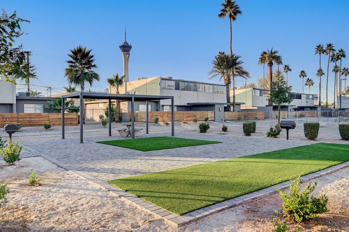 Scenic apartment courtyard featuring a modern gazebo, lush greenery, and iconic city skyline views with towering palm trees.