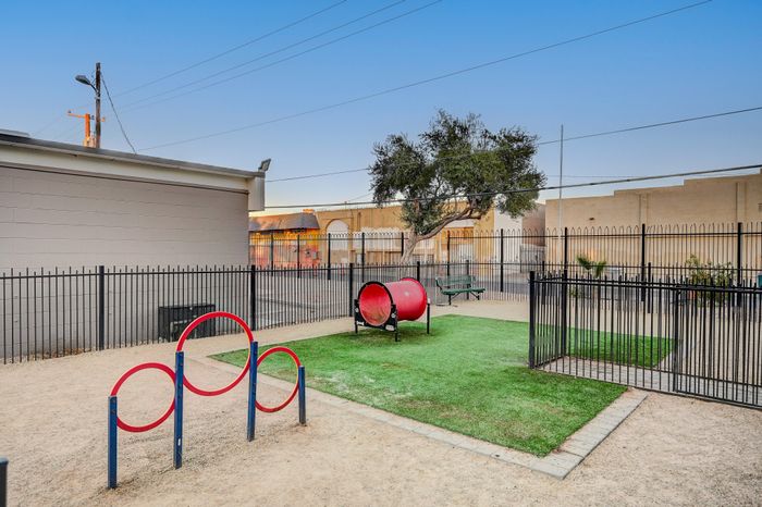 Charming fenced-in play area featuring bright red play equipment and lush green grass, perfect for a family-friendly atmosphere.
