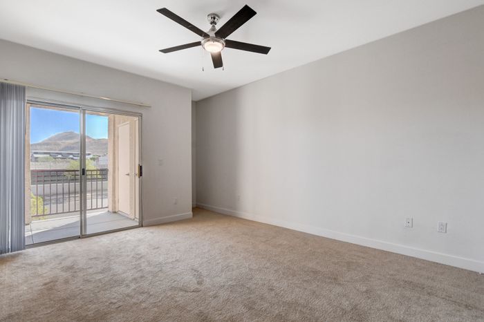 Bright and spacious empty room with a ceiling fan and large sliding doors leading to a balcony with mountain views.