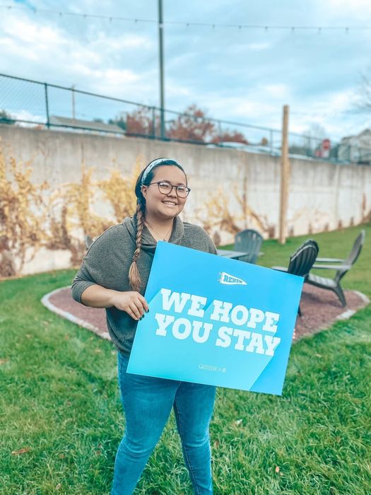 A person holding a blue sign saying we hope you stay