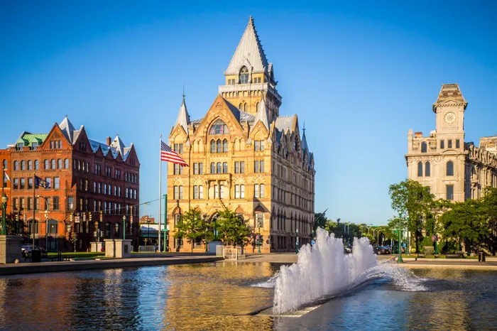 A historic building near the Campus West apartment complex in Syracuse, featuring a pond with a fountain in it.