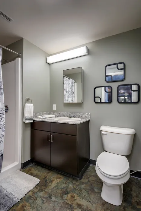 Model bathroom at our apartments for rent in Syracuse, featuring wood grain cabinetry and white countertops.