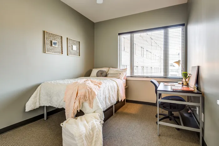 Model bedroom with furniture and a large window at Campus West apartments near Syracuse University.