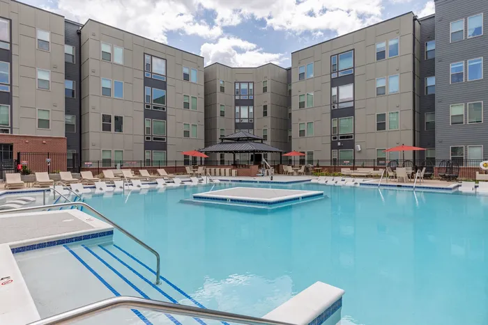 The pool deck at our student apartments for rent in Blacksburg, featuring beach chairs, umbrellas, and a shade structure.
