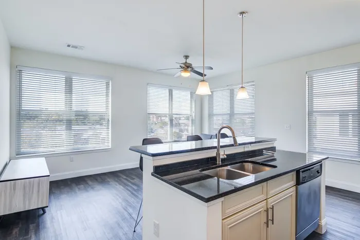 Empty living room at our student apartments in Storrs, featuring carpeted flooring and a view of the kitchen.