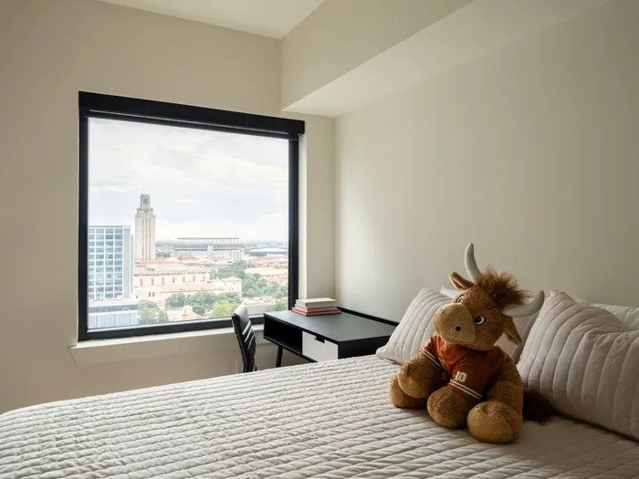 Model apartment bedroom at Union on 24th with full size bed, desk, and chair with a large window looking out at the city of Austin, TX.