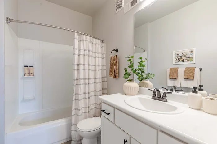 Model apartment bathroom with hardwood flooring, white cabinets, and white bathroom facilities
