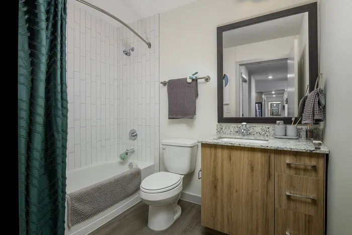 model apartment bathroom with wood cabinets and white bathroom facilities, including a bathtub.