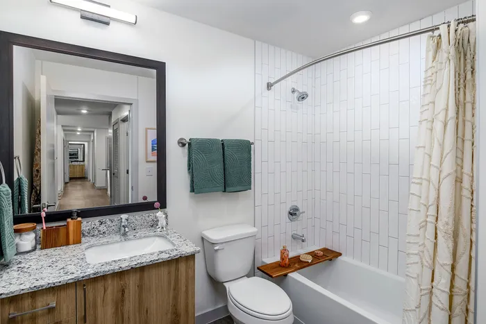 model apartment bathroom with wood cabinets and white bathroom facilities, including a bathtub.
