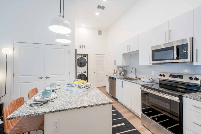 Model apartment kitchen with granite counter tops, white cabinets, and stainless steel appliances at The Accolade Collegiate Village East Orlando apartments.