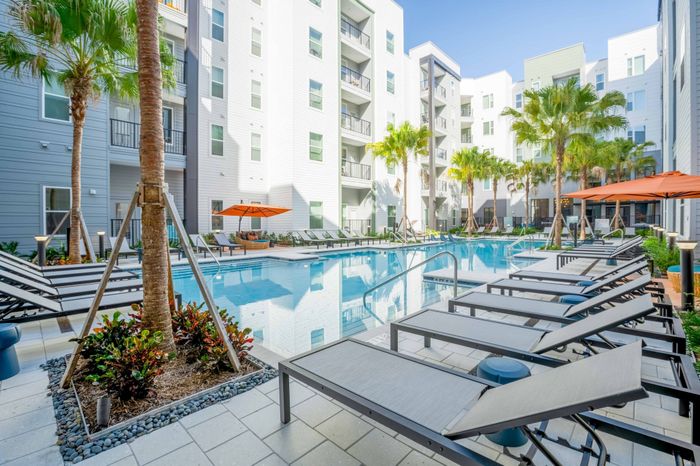 Sparkling pool with sun loungers and orange umbrellas lining the pools edge at The Accolade Collegiate Village East Orlando apartments.