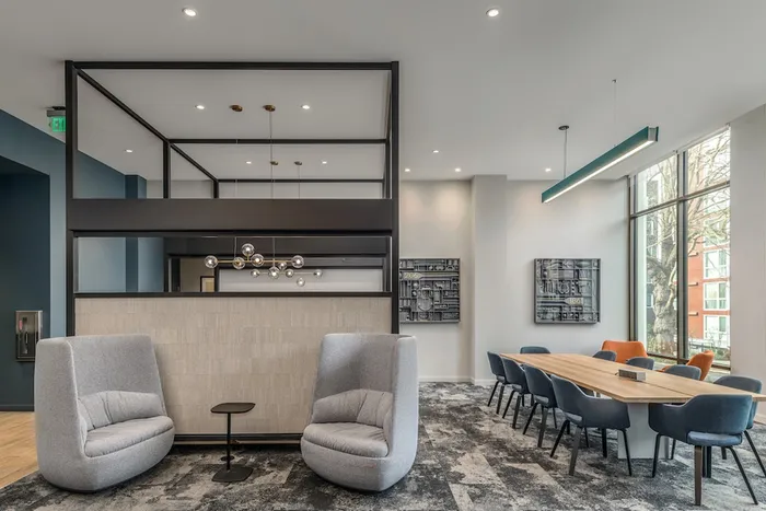 Common lounge at our apartments in Seattle, featuring carpeted floors, cushioned chairs, and large windows.