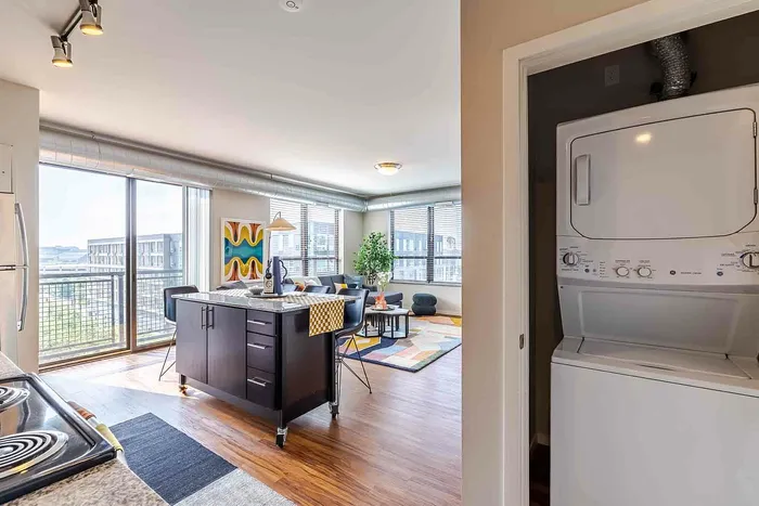 Photo of the stackable washer & dryer in a closer with views of the living room in the background