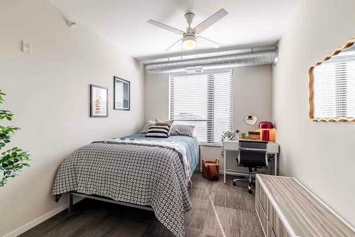 Model unit bedroom with a full size bed, dresser, desk, chair, and a large window