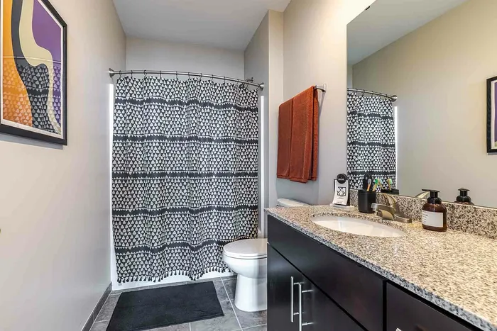Model unit bathroom with granite countertops, dark brown cabinets, and white bathroom facilities