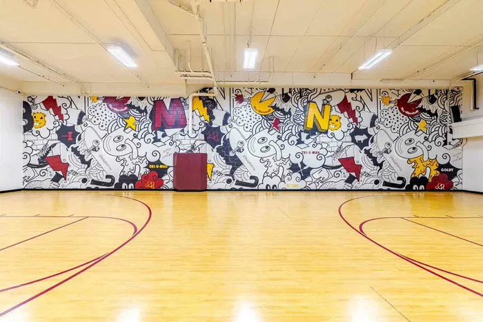 Full size indoor basketball court with a black, white, maroon, and gold mural on the wall