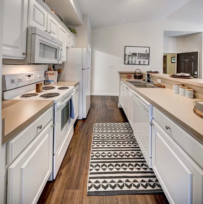 Modern kitchen with sleek white cabinetry, stylish appliances, and elegant hardwood flooring, complemented by a decorative runner rug and ample countertop space.