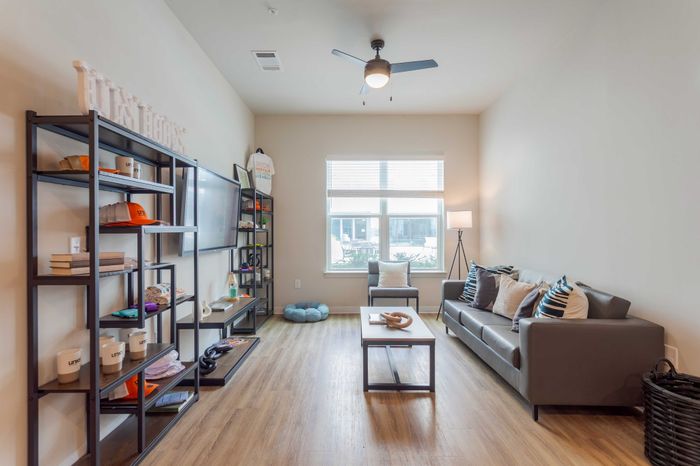 Inviting living room with modern decor, featuring sleek shelves, cozy seating, and abundant natural light from large windows.