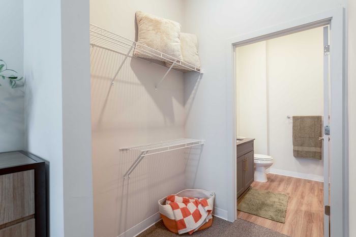Chic apartment nook featuring an organized storage area with plush pillows on a wire rack and a warm bathroom view with modern fixtures.