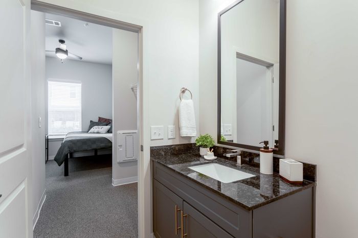 Modern bathroom with sleek granite countertop, elegant mirror, and cozy bedroom view in a stylish apartment.