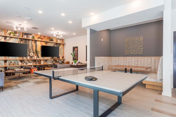 Modern entertainment room with elegant decor, featuring a sleek ping pong table, comfortable sofa seating, and artistic wall design with dual flat-screen displays.