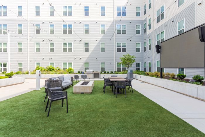 Modern apartment courtyard featuring a spacious outdoor seating area with stylish furniture, lush green artificial turf, and high-rise windows.