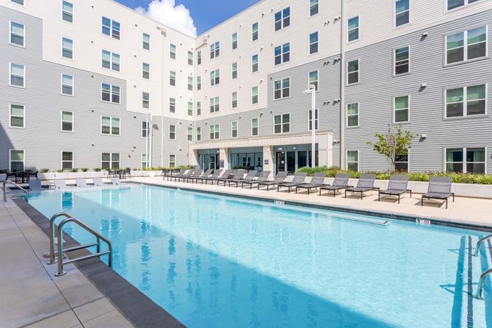 Modern apartment complex featuring a refreshing outdoor pool with ample sun loungers for relaxation.