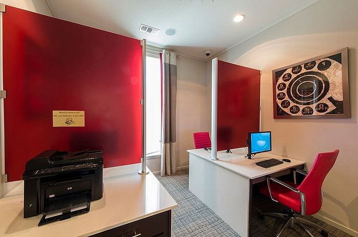 Modern home office with vibrant red accents, featuring a dual workspace setup, comfortable seating, and a sleek printer station.