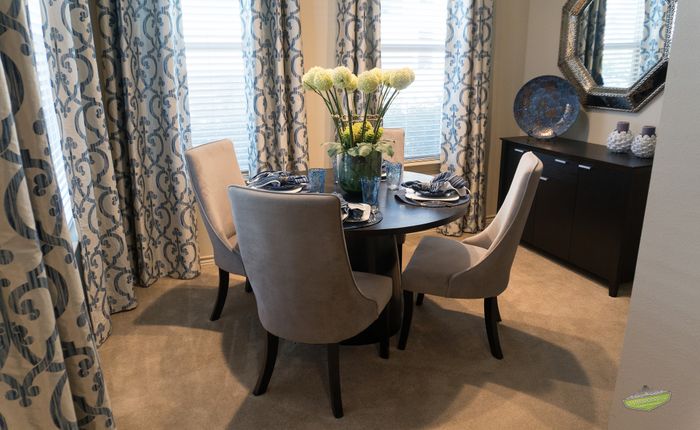 Elegant dining area with a round table set for four, featuring chic upholstered chairs and a stylish centerpiece, accented by luxurious patterned drapes.