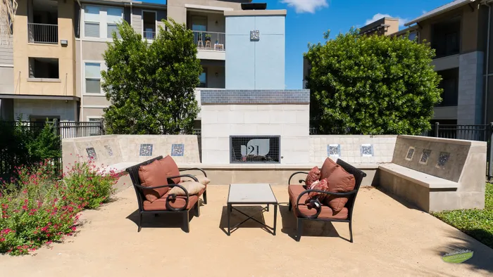 Charming outdoor patio with cozy armchairs, vibrant greenery, and a modern fireplace, perfect for relaxing and entertaining.
