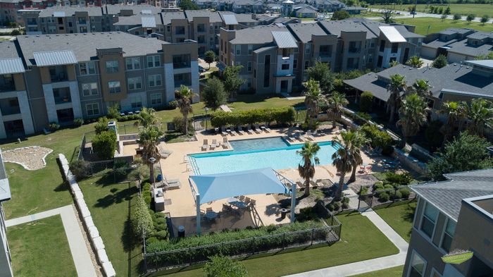 Modern apartment complex with a sparkling outdoor pool surrounded by palm trees and lush greenery, offering a resort-style living experience.