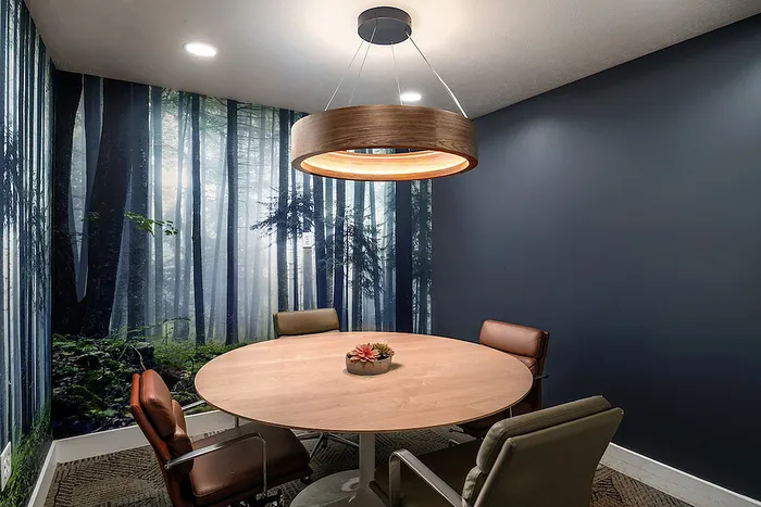 Modern meeting room with a round wooden table, four stylish chairs, and a serene forest mural enhancing the ambiance.