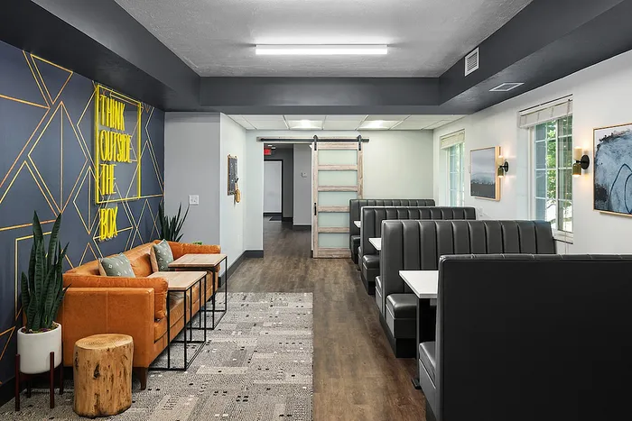 Modern communal lounge featuring a cozy leather sofa, vibrant wall decor, and elegant booth seating perfect for social gatherings.