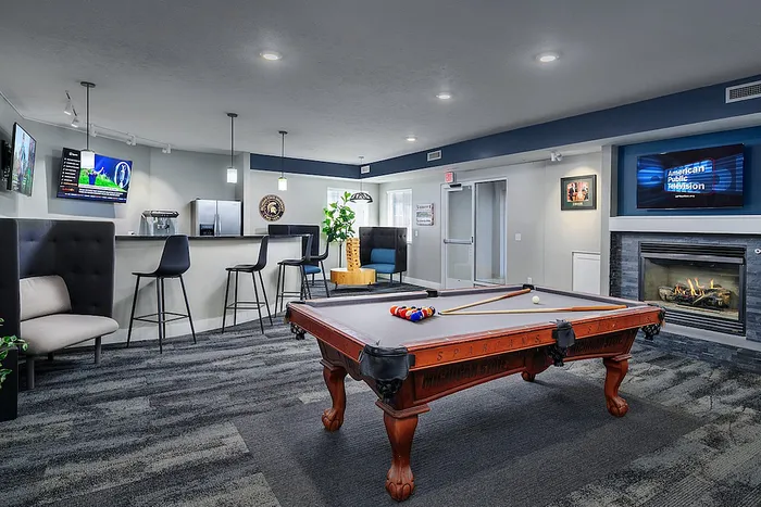 Luxurious game room with a stylish billiard table, cozy seating, modern bar area, and ambient fireplace.